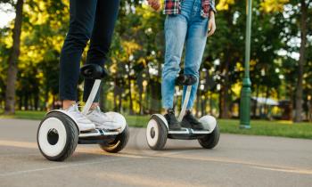 Male and female person riding on gyro board in park. Outdoor recreation with electric gyroboard. Transport with balance technology