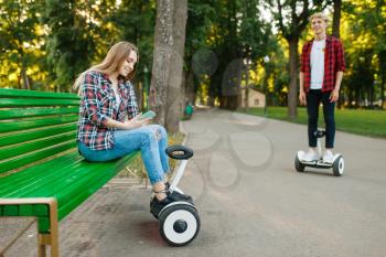 Young couple leisures with gyro board in summer park. Outdoor recreation with electric gyroboard. Transport with balance technology