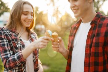 Young love couple feed each other ice cream in summer park. Boyfriend and girlfriend leisures together with ice-cream, romantic walk