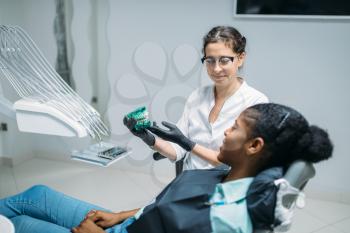 Female dentist shows dentures to woman in a dental chair, professional dentistry, stomatology cabinet