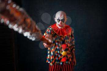 Scary bloody clown reaches out baseball bat. Man with makeup in halloween costume, crazy killer