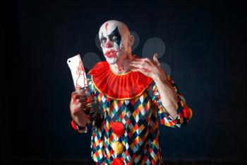 Mad bloody clown with meat cleaver, circus horror. Man with makeup in carnival costume, crazy maniac
