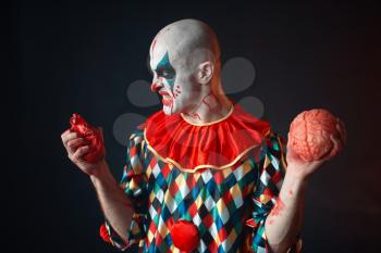 Mad bloody clown holds human heart and brain. Man with makeup in carnival costume, crazy maniac 