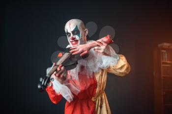 Scary bloody clown plays the violin with a human hand. Man with makeup in carnival costume, mad maniac, crazy killer