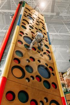 Little girl climbing walls in children game center, bottom view. Excited child having fun on playground indoors