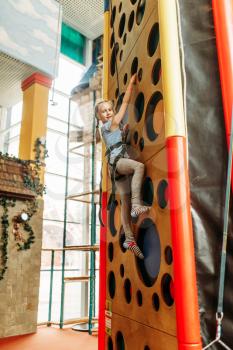 Funny girl climbing walls in children game center. Excited child having fun on playground indoors. Female kid playing in amusement centre, activity attraction