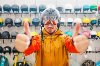 Man in helmet for ski or snowboarding shows thumbs up, side view, sports shop. Winter season extreme lifestyle, active leisure store, buyers choosing protect equipment