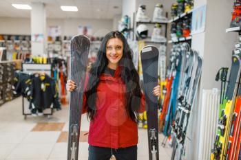 Woman at the showcase holding downhill ski in his hands, front view, shopping in sports shop. Winter season extreme lifestyle, active leisure store, buyer choosing skiing equipment