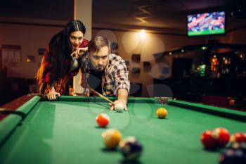 Family couple plays in billiard room. Man and woman leisures, american pool game in sport bar, male player aiming to shot