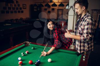 Woman learn to play billiard, poolroom on background. Couple hobby, american pool game, female player aiming to shot