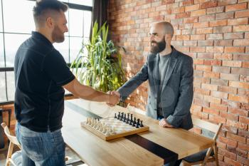 Chess players shake hands before the game. Two male chessplayers begin the intellectual battle indoors. Chessboard on wooden table