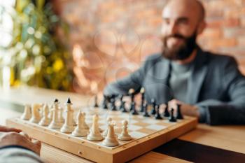 Male chess players begin playing, focus on board with figures. Two chessplayers begin the intellectual tournament indoors. Chessboard on wooden table, strategy game