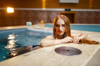 Sexy lady poses at the side of the pool indoors. Swimming and relaxation, healthy lifestyle, spa therapy and body care