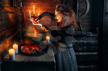 Scary witch cooking soup with human body parts, dark powers of witchcraft, spiritual seance with candles. Female foreteller calls the spirits, terrible future teller