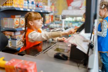 Cute girl in uniform at the cash register playing saleswoman, playroom. Kids plays sellers in imaginary supermarket, salesman profession learning
