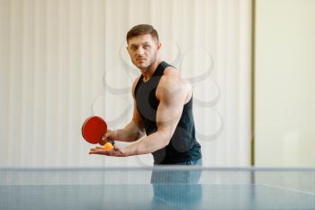 Man with ping pong racket preparing to hit a ball, workout indoors. Male person in sportswear, training in table tennis club