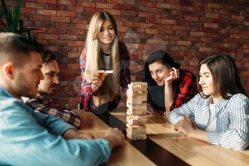 Smiling friends plays table game at home, selective focus on tower. Board game with wooden blocks requiring high concentration, entertainment for funny company