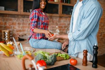 Black couple cooking together on the kitchen. African family preparing vegetable salad at home. Healthy vegetarian lifestyle