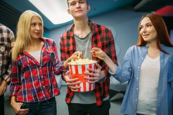 Group of friends with popcorn stands in cinema hall before the screening. Male and female youth in movie theater