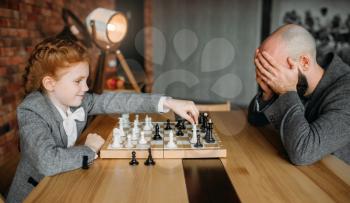 Cute schoolgirl playing chess with adult male person. Young girl at the chessboard, female kid plays logic game
