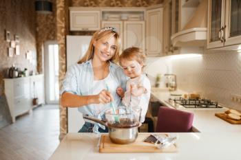 Young mother with her daughter mixing melted chocolate in a bowl. Cute woman and little girl cooking on the kitchen. Happy family prepares sweet dessert at the counter