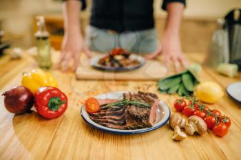 Plate wit roasted meat slices on wooden table, Male chef and fresh cooked dish for gourmets, kitchen on background. Man preparing beef with vegetables on countertop