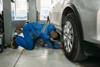 Repairman in uniform adjusts lift jack in car service, suspension diagnostic. Automobile service, vehicle maintenance