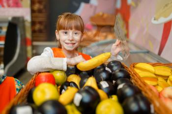 Smiling little girl in uniform playing saleswoman, playroom. Kids plays fruit sellers in imaginary supermarket, salesman profession learning
