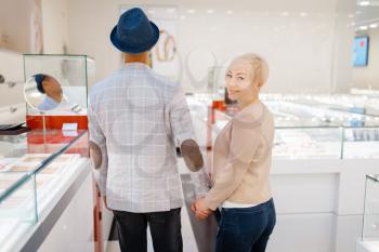 Love couple buying jewels in jewelry store, back view. Man and woman choosing wedding rings. Future bride and groom in jewellery shop