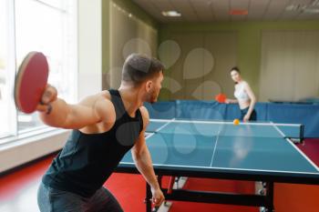 Man and woman playing ping pong indoors, focus on racket. Couple in sportswear plays table tennis in gym