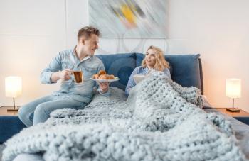 Love couple having romantic breakfast in bed with croissants and cookies. Man and woman eats dessert in bedroom, good morning. Happy lifestyle, beautiful relationship