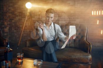Woman in shirt and trousers reading newspapar with whiskey and cigar, retro fashion, gangster style. Vintage business lady
