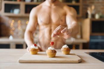 Man with naked body cooking cakes with cherry on the kitchen. Nude male person preparing breakfast at home, food preparation without clothes