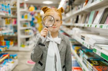 Little schoolgirl choosing magnifying glass, shopping in stationery store. Female child buying office supplies in shop, schoolchild in supermarket