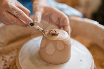Female potter removes the extra layer on pot, pottery wheel. Woman molding a bowl. Handmade ceramic art, tableware from clay