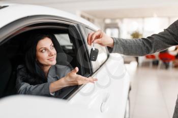 Happy woman takes the key to the new car in showroom. Female customer buying vehicle in dealership, automobile sale