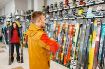 Man at the showcase choosing downhill ski, shopping in sports shop. Winter season extreme lifestyle, active leisure store, customer buying skiing equipment