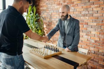 Chess players shake hands before the game. Two male chessplayers begin the intellectual battle indoors.