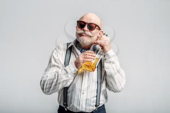 Fashionable elderly man hugs the bottle of good alcohol, grey background. Mature senior looking at camera in studio, dude