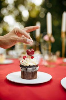 Table setting, tea party, woman decorate cakes with fresh cherry. Luxury silverware on red tablecloth, tableware outdoors. Wedding celebration on summer meadow