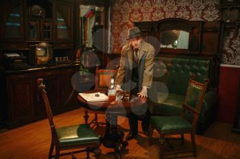 Male detective in hat and coat at the crime scene, retro style. Criminal investigation, inspector search evidence, vintage room interior on background