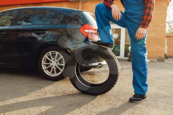 Male worker in uniform poses with tyre, tire service. Vehicle repair service or business, man change wheels on automobile outdoor
