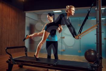 Slim woman in sportswear and instructor, pilates training with ball on exercise machine in gym. Fitness workuot in sport club. Athletic female person, aerobics indoor, body stretching