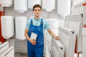Plumber in uniform choosing water heating radiator at showcase in plumbering store. Man buying sanitary engineering in shop