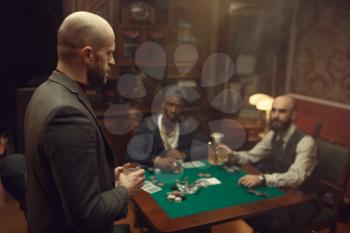 Three poker players with whiskey and cigars sitting at the table. Games of chance addiction, gambling house,