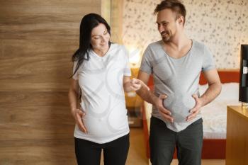 Happy couple, pregnant wife with belly at home, bedroom interior on background. Pregnancy, prenatal period. Expectant mom and dad are resting on sofa, health care