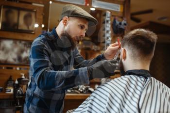 Barber with comb and scissors makes a haircut to a client. Professional barbershop is a trendy occupation. Male hairdresser and customer in retro style hair salon