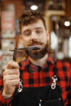Barber shows razor blade. Professional barbershop is a trendy occupation. Male hairdresser in retro style hair salon, accessories for cutting