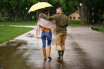 Love couple drinks hot coffee in park, summer rainy day. Man and woman stand under umbrella in rain, romantic date on walking path, wet weather in alley