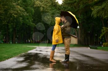 Happy love couple swears to each other in park, summer rainy day. Man and woman under umbrella in rain, romantic date on walking path, wet weather in alley